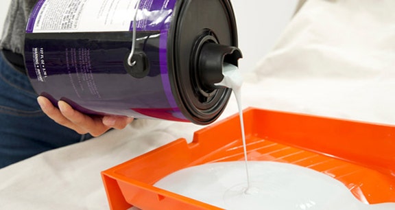 Person pouring paint of the simple pour lid spout into a paint tray