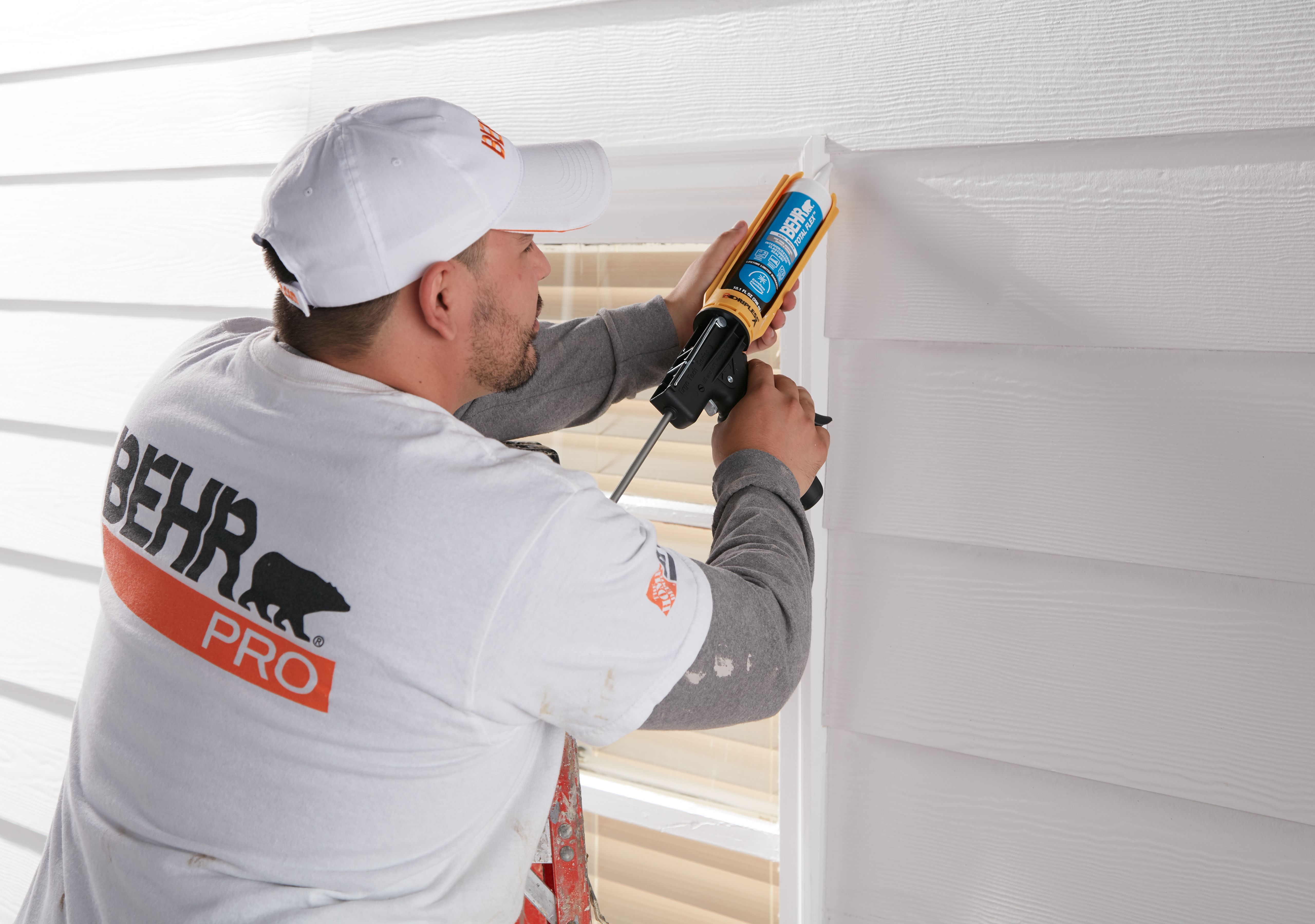 Painting professional wearing Behr Pro gear sealing an exterior surface